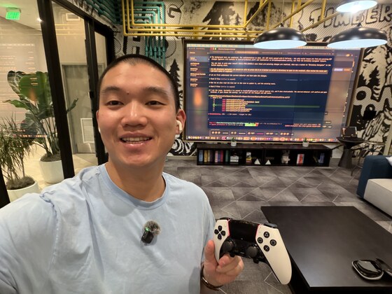 Kevin holding a DualSense controller in front of a wall-mounted display running a terminal — vibe coding with ControllerKeys